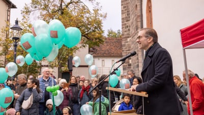 Person am Rednerpult vor einer Menschenmenge mit Luftballons.