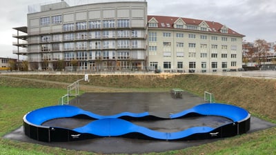 Skatepark mit blauem Wellenkurs vor Gebäuden.