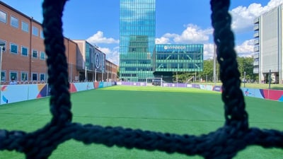 Fussballfeld mit Blick durch das Netz auf ein modernes Gebäude.