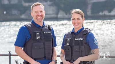 Zwei Polizisten in blauen Uniformen vor einem Fluss.