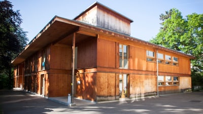 Holzgebäude mit Fenstern, umgeben von Bäumen.