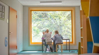 Zwei Kinder sitzen an einem Tisch vor einem grossen Fenster.