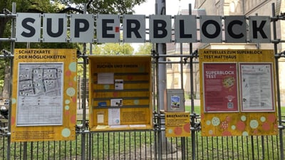 Informationsschilder mit 'Superblock' über einem Zaun vor einer Kirche.