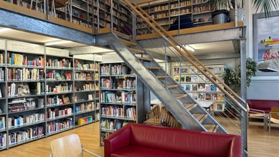 Moderne Bibliothek mit roten Sofas und Metalltreppe.
