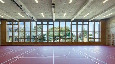 Turnhalle von Innen, mit einer grossen Fensterfront und rotem Boden.