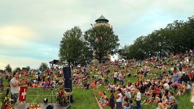 Menschenmenge bei Veranstaltung auf Wiese mit Wasserturm im Hintergrund.