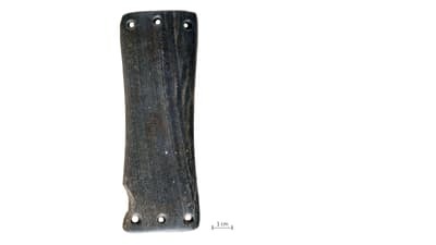 Steinzeitliche Armschutzplatte aus Stein mit mehreren Löchern auf weissem Hintergrund und Massstab 1cm