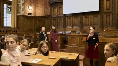 Frauen und Kinder in einem Holzsaal, eine Frau hält ein Mikrofon.