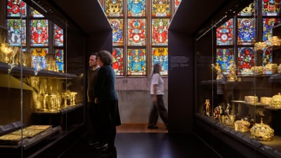 Zwei Personen betrachten Ausstellungsstücke in einem Museum mit farbigem Glasfenster.