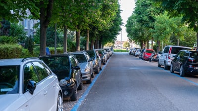 Baumgesäumte Strasse mit geparkten Autos in einem Basler Quartier.