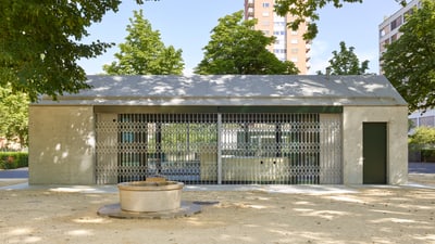 Pavillonartiges kleines Gebäude mit geöffneter Fensterfront, die gleichzeitig als Ein-/ Durchgang dient, welche mit einem Gitter verschlossen ist.