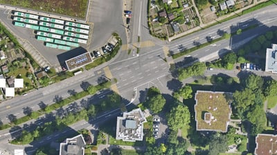 Luftaufnahme einer stark befahrenen Strassenkreuzung mit umliegenden Gebäuden und Grünflächen.