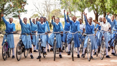 Gruppe von Schülern in blauen Uniformen mit Fahrrädern, jubelnd im Freien.