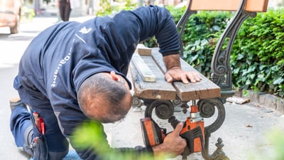 Mann repariert Parkbank mit Bohrmaschine.