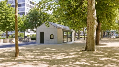 Kindertankstelle im Park von Bäumen und Wegen umgeben, dahinter wird ein Wohnblock sichtbar.