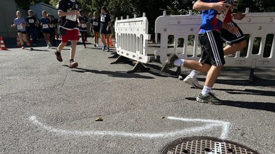 Menschen rennen auf einer Strasse mit Absperrungen und Richtungspfeil.