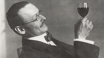 Hermann Hesse mit Brille betrachtet Weinglas.",