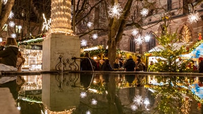 Weihnachtsmarkt mit Lichtern, Reflexionen im Wasserbecken.",