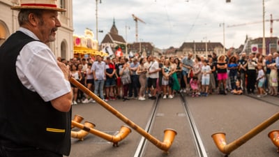 Person mit Alphorn vor einer Menschenmenge auf der Strasse.