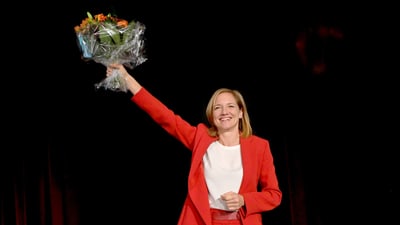 Frau in rotem Anzug hält Blumenstrauss mit Lächeln.",