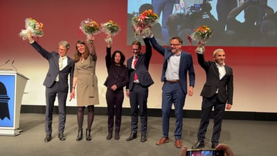 Gruppe lächelnder Menschen mit Blumensträussen auf der Bühne.",