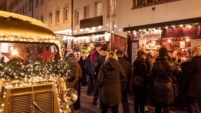 Foule sur un marché de Noël avec des stands décorés.