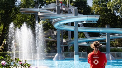 Person im roten Shirt vor Wasserrutsche und Springbrunnen.