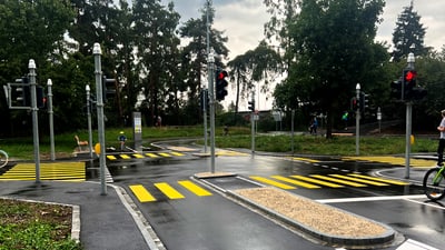 Übungsverkehrsfläche mit Ampeln und Zebrastreifen vor Bäumen.