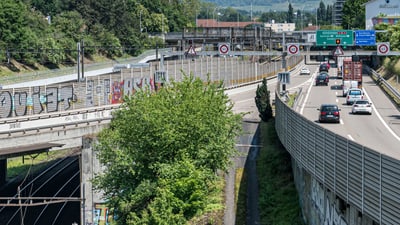 Stadtstrasse neben Bahngleisen mit Verkehr und Graffiti.