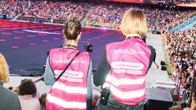 Zwei Personen mit Opferhilfe-Westen bei Veranstaltung im Stadion.
