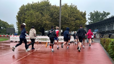 Gruppe von Läufern auf nasser roter Laufbahn bei Regen.