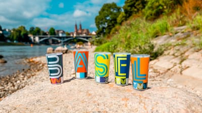 Bunte Becher mit 'Basel' am Flussufer in der Sonne