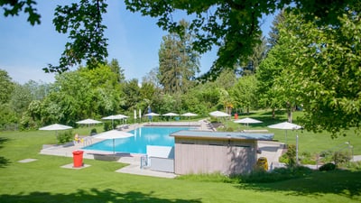 Freibad mit grüner Umgebung und Sonnenschirmen.