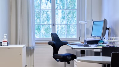 Büro mit Schreibtisch, Stuhl und Fenster mit Blick ins Freie.