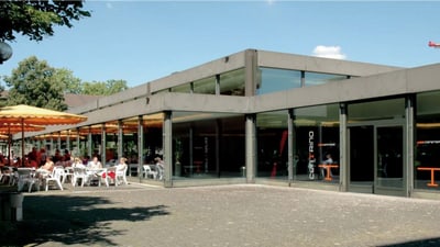 Aussenansicht eines Cafés mit Terrasse und Gästen.