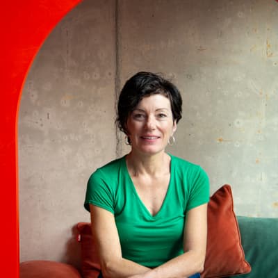 Andrea Grasser sitzt vor rotem Bogen auf Kissen, lächelnd.