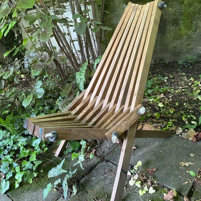 Holzstuhl im Garten auf Pflastersteinen und Laub.