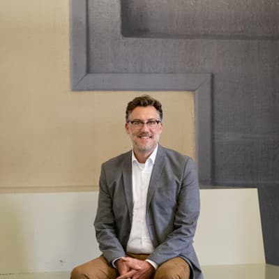 Patrick Langloh sitzt auf einem weissen Sofa vor geometrischem Wandbild.