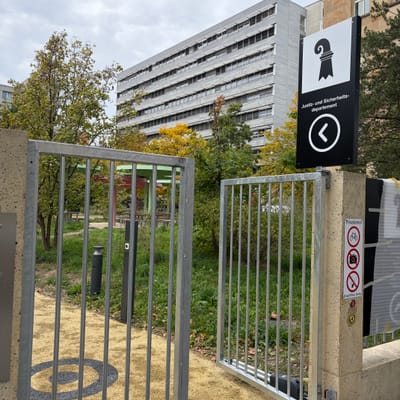 Geöffneter Eingang mit Schild vor einem modernen Gebäude.