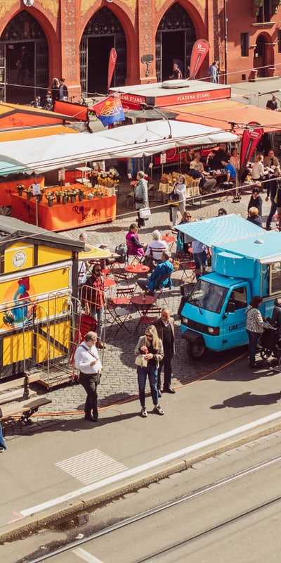 Marktstände und Menschen an einer belebten Strassenszene.