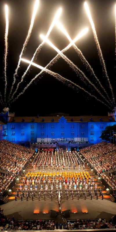 The Kaserne Basel is filled with people in the stands and on the stage. A spectacle of light plays out in the dark sky.