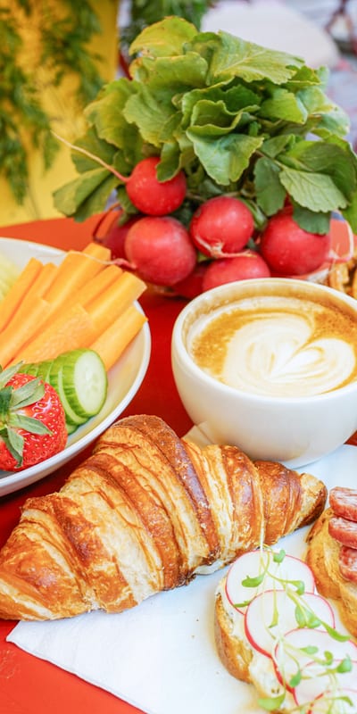 Frühstückstisch mit Croissant, Kaffee, Obst, Gebäck und Radieschen.