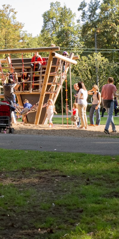 Kinder und Erwachsene im Park bei einem Spielplatz mit Holzkonstruktion.