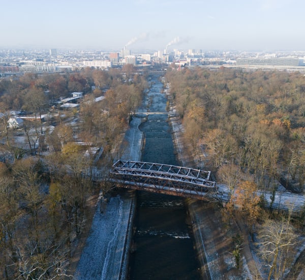 Luftaufnahme einer Brücke über einen Fluss mit Stadt im Hintergrund.