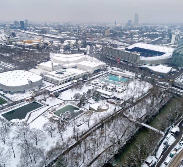 Luftaufnahme einer schneebedeckten Stadtlandschaft mit Fluss und Stadion."  