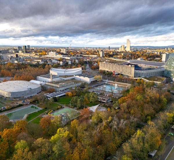 Luftaufnahme einer Stadt mit Hochhäusern, Parks und bewölktem Himmel.