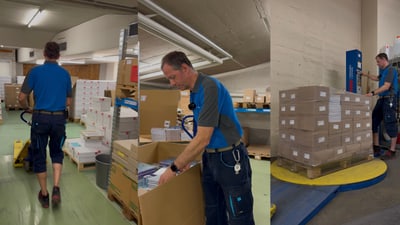 Mann in blauer Arbeitskleidung in Lagerhalle mit Kartons.