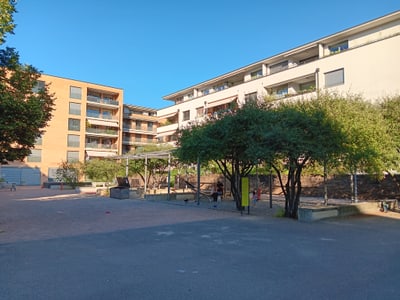 Wohnanlage mit Bäumen und Spielplatz im Vordergrund.