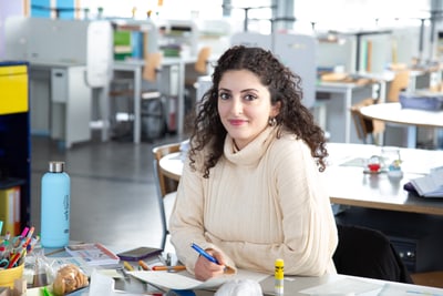 Tanya Matur sitzt an Tisch mit Papier und Stiften im Büro.