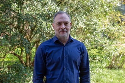 Mann in blauem Hemd vor grünem Hintergrund im Freien.